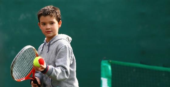 Poika kädessään tennismaila ja tennispallo